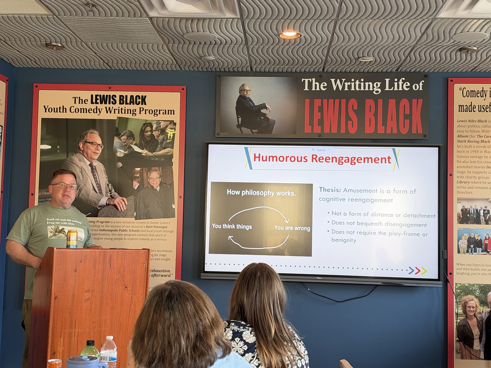 A presenter at the lectern with a slide titled 
