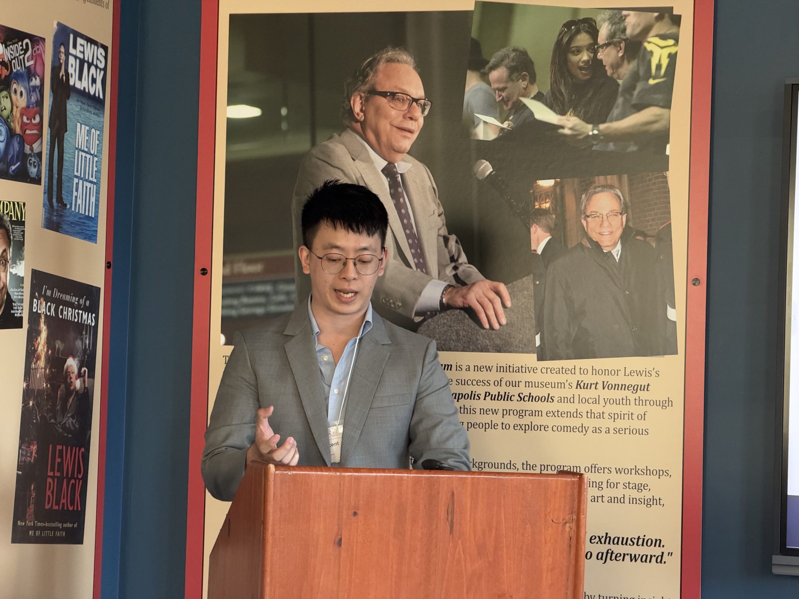 A presenter speaking at the lectern in front of Lewis Black exhibit panels