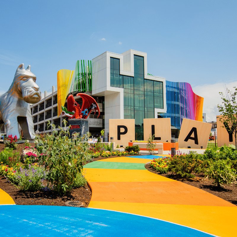 The Strong National Museum of Play, with a colorful path, a large silver dog sculpture, a red dragon, and giant letters spelling PLAY